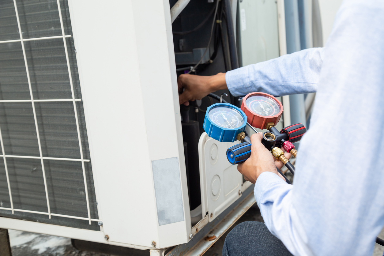 Air repair mechanic using measuring equipment for filling industrial factory air conditioners and checking maintenance outdoor air compressor unit. Air repair mechanic using measuring equipment for filling industrial factory air conditioners and checking maintenance outdoor air compressor unit.