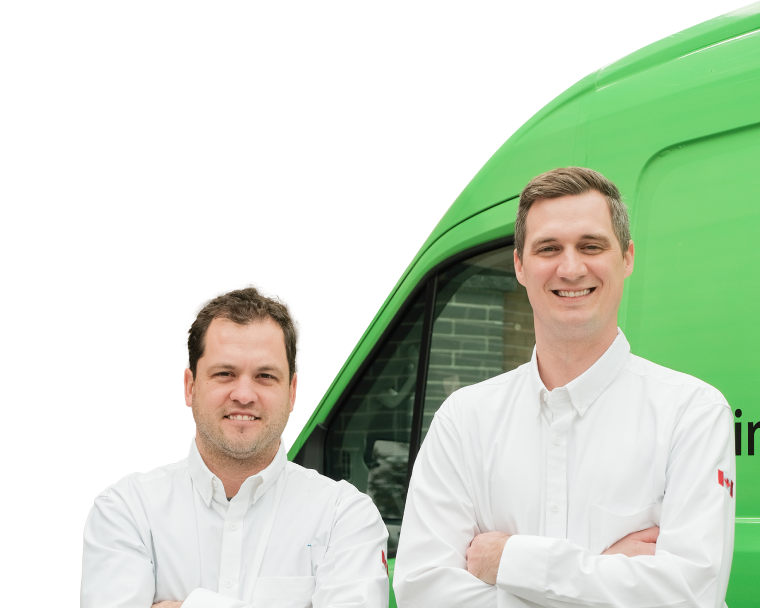 Two Mr. Furnace technicians smiling in front of their green service van, wearing issued jackets during an on-site consultation.