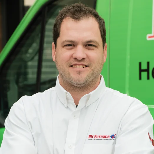 mr_furnace-individual Smiling Mr. Furnace technician standing confidently in front of their green service van, wearing their white issued uniform.