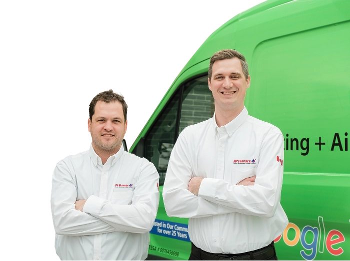 Two Mr. Furnace technicians smiling in front of their green service van, wearing issued jackets during an on-site consultation.