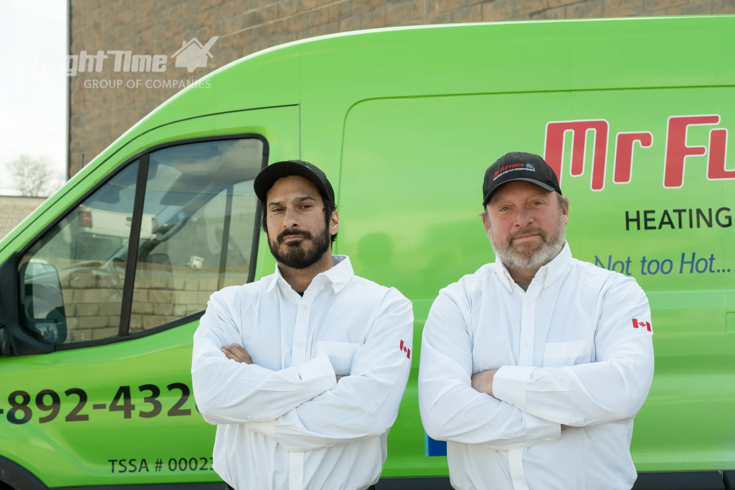 Two Mr. Furnace technicians are standing with arms crossed in front of a green service van.